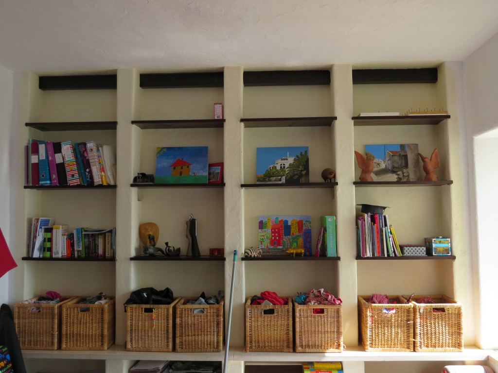 En hel vägg med platsbyggda hyllor utgör en spännande fond som kan varieras i det oändliga. I korgarna som komemr från möbelvaruhuset och som visade sig passa perfekt på millimenterna i hyllan förvaras kläder som är bra att ha till hands. Konstverk spapade av barnen och morfar pryder hyllorna. En kombination av walk-in-closet, galleri och bibliotek.